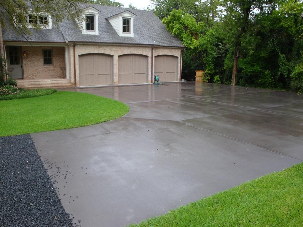 A concrete driveway leading to a large house with three garage doors.