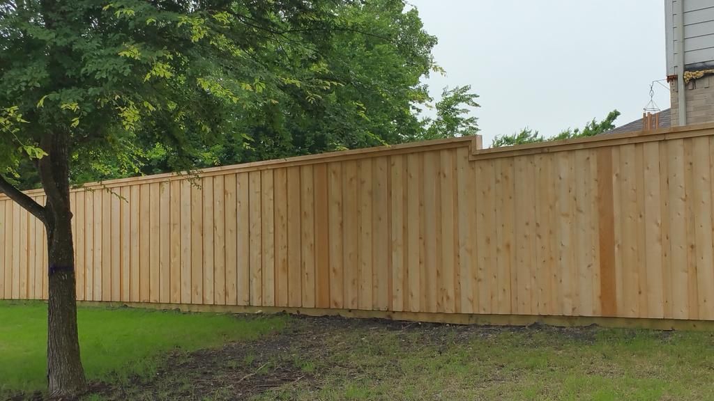 A wooden fence is surrounded by grass and trees in a backyard.