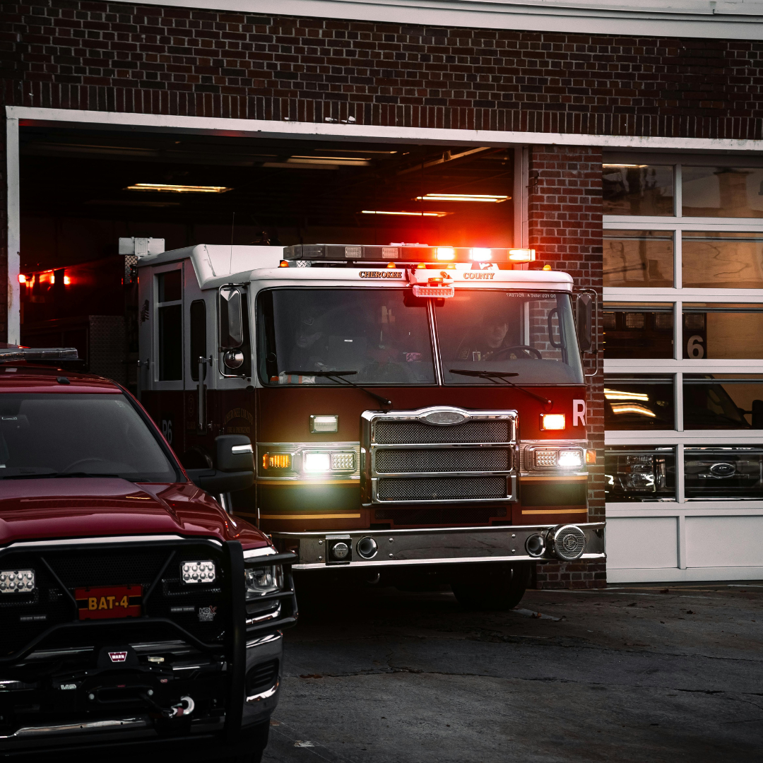 Fire truck and SUV parked outside a brick fire station; emergency lights on.