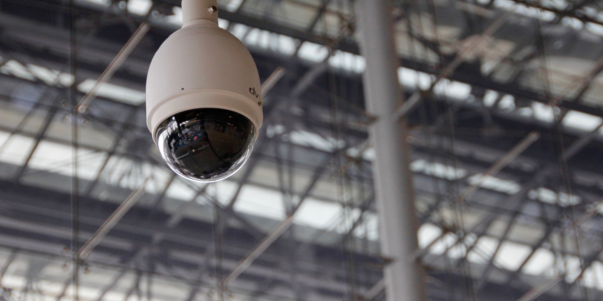 White dome security camera hanging from a ceiling in an indoor industrial space