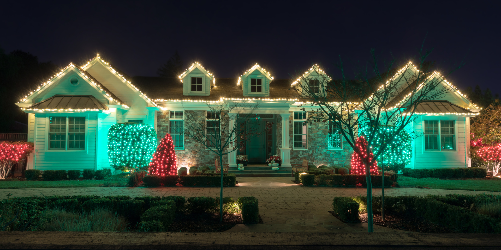 A house decorated with Christmas lights at night, with green and red lights, and lit-up trees.