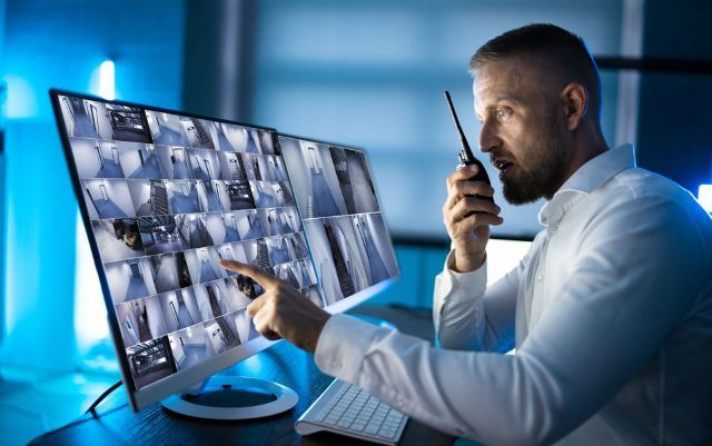 A man is talking on a walkie talkie while looking at a computer screen.