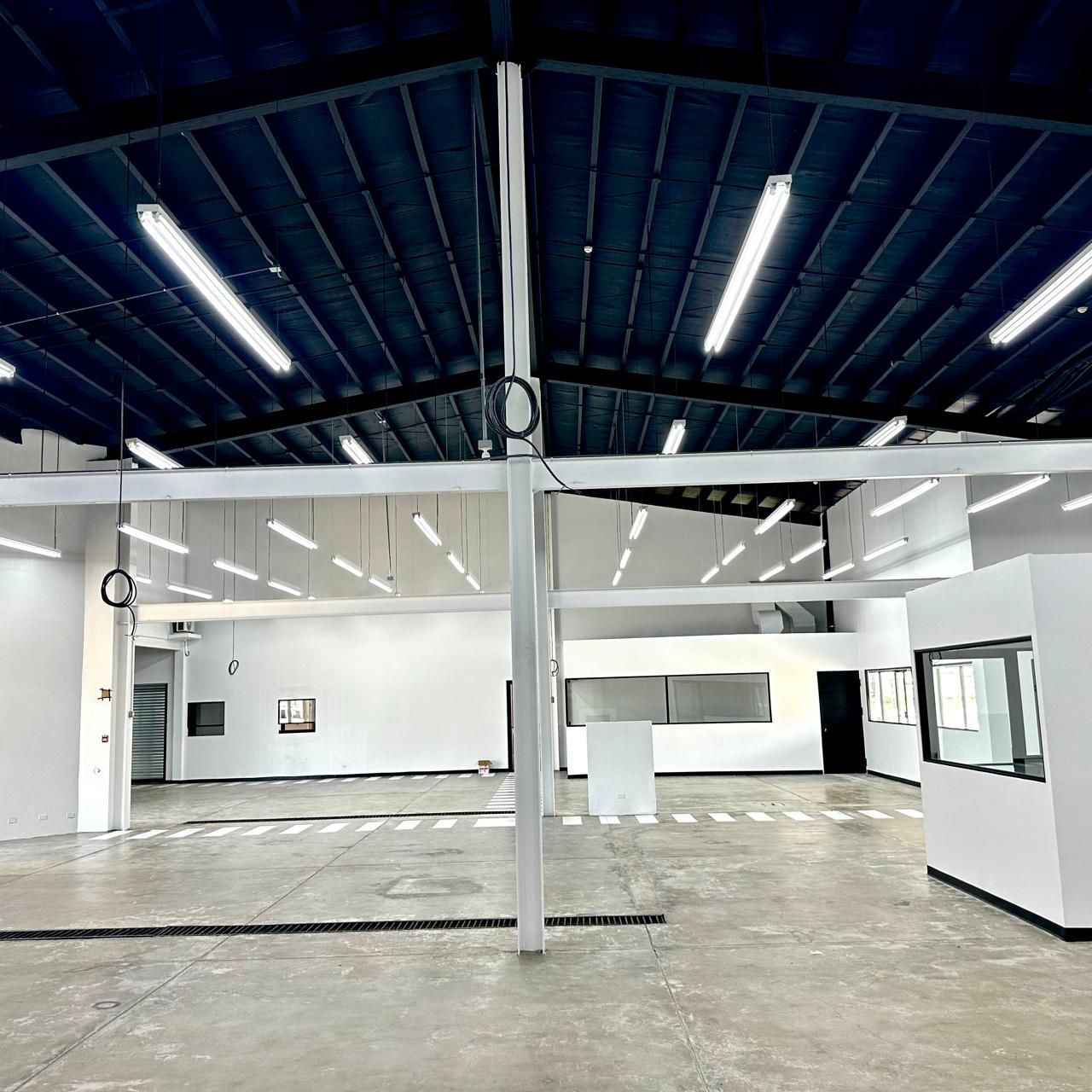 Empty white-walled industrial space with high ceilings, fluorescent lights, and a concrete floor.