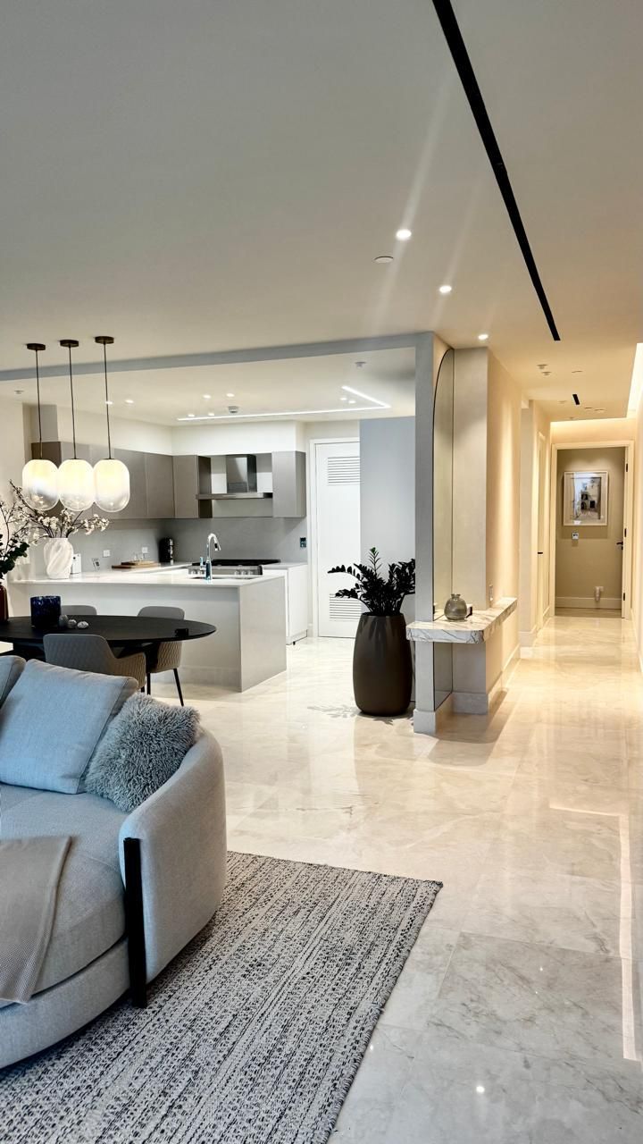 Modern, open-plan apartment interior with kitchen, living area, and hallway. Light tones, marble floors, and contemporary decor.