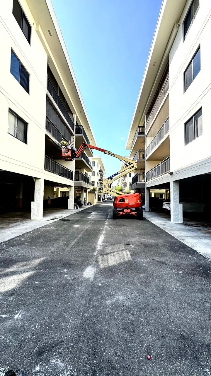 A cherry picker working on a building's facade, with a work vehicle parked in the alley below, under a blue sky.