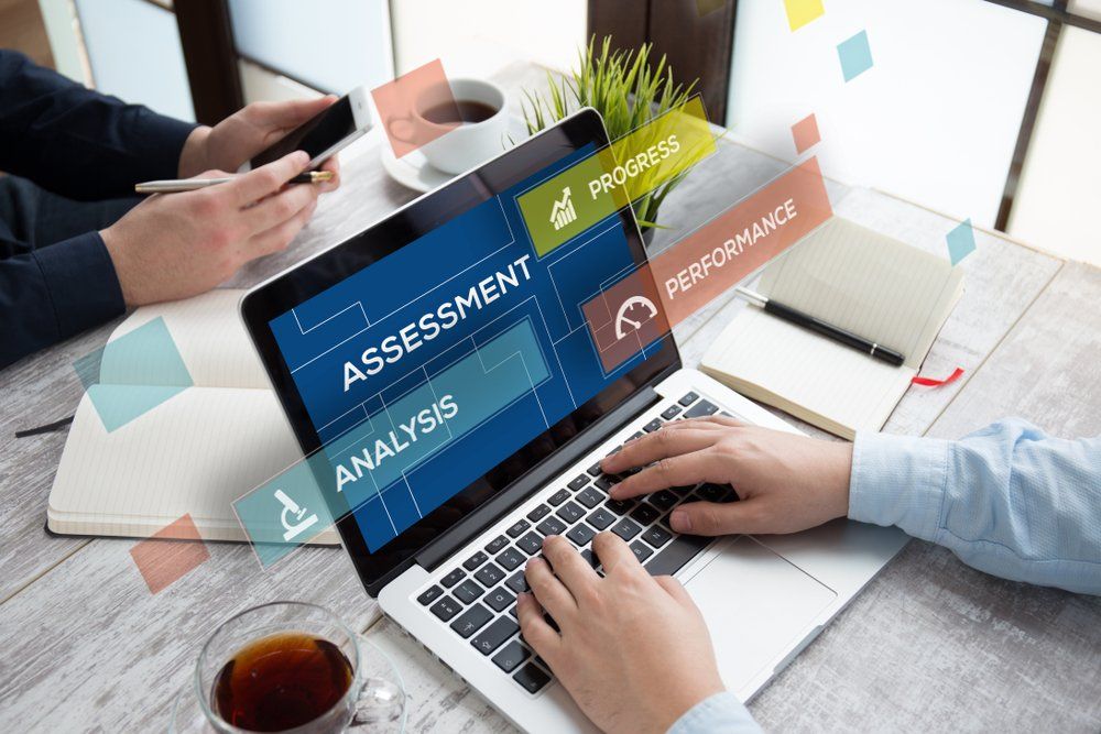 A person is typing on a laptop computer with the word assessment on the screen.