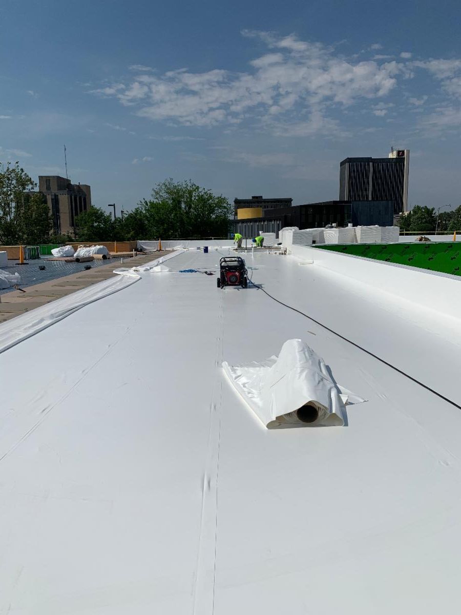 A bright white membrane roof installation in progress with a heat-welding machine on a flat rooftop under a blue sky.