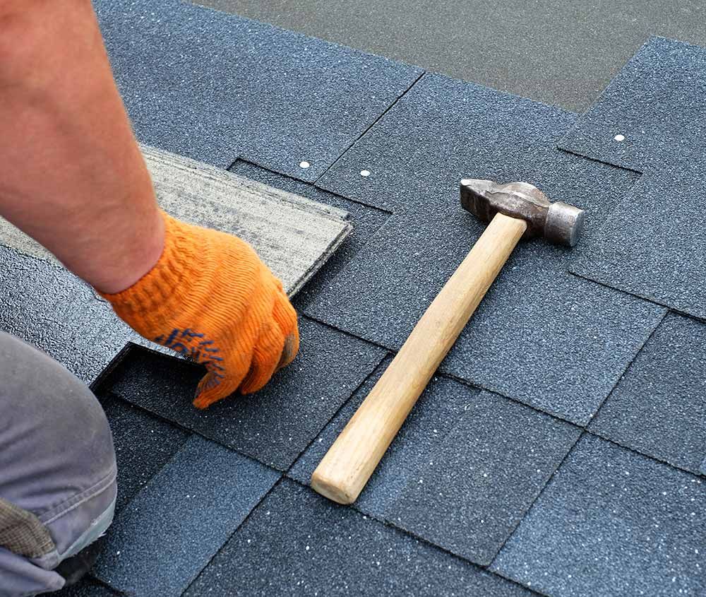 a person is installing shingles on a roof with a hammer .