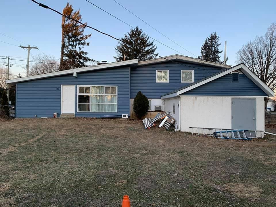 a blue house with a white garage and a ladder in front of it