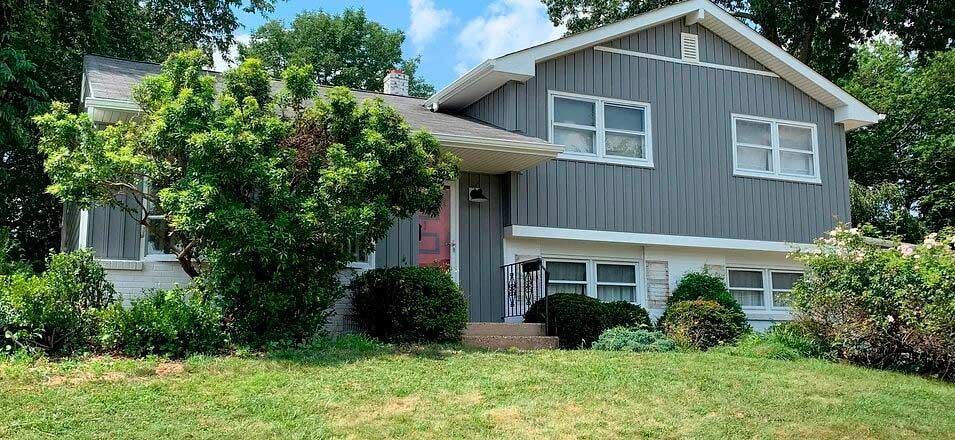 a large house with a gray siding and white trim is sitting on top of a lush green lawn .
