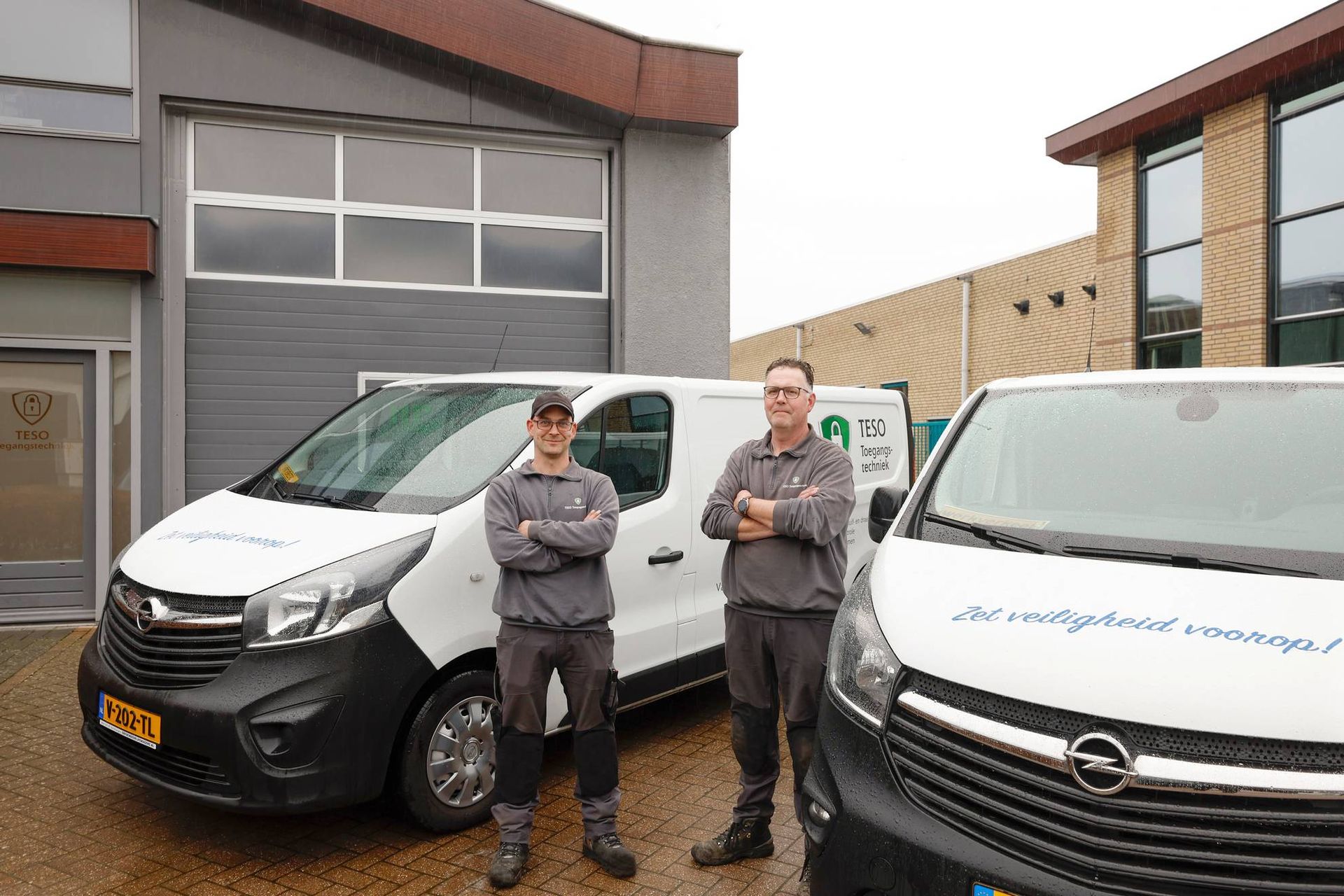 Twee mannen staan ​​naast twee busjes voor een gebouw.