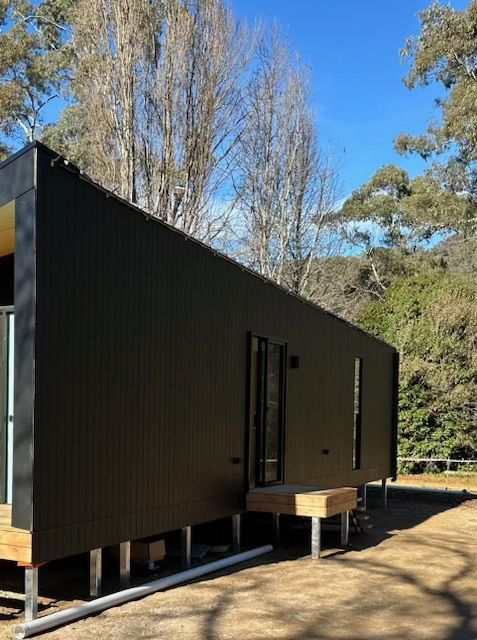 A Small Black House is Sitting on Top of a Dirt Field Next to Trees — Skyline Painting In Lavington, NSW