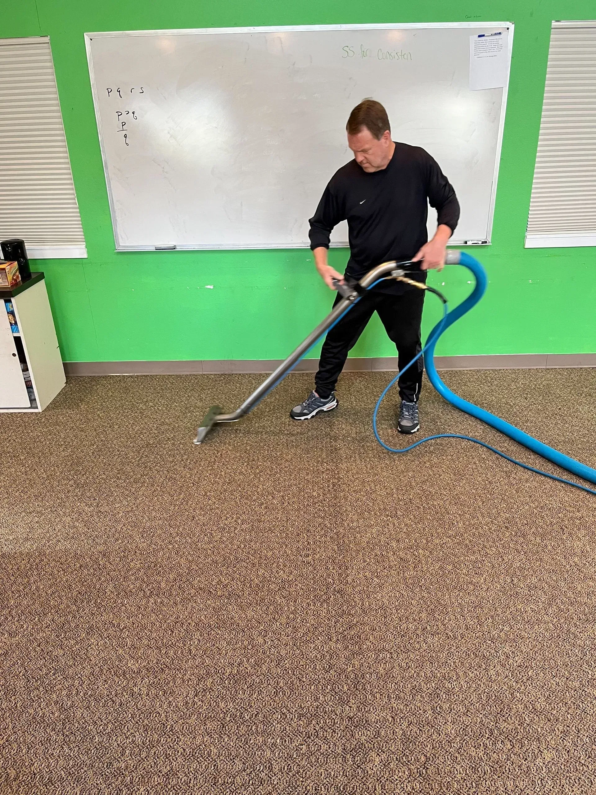 A man is cleaning a carpet with a vacuum cleaner.