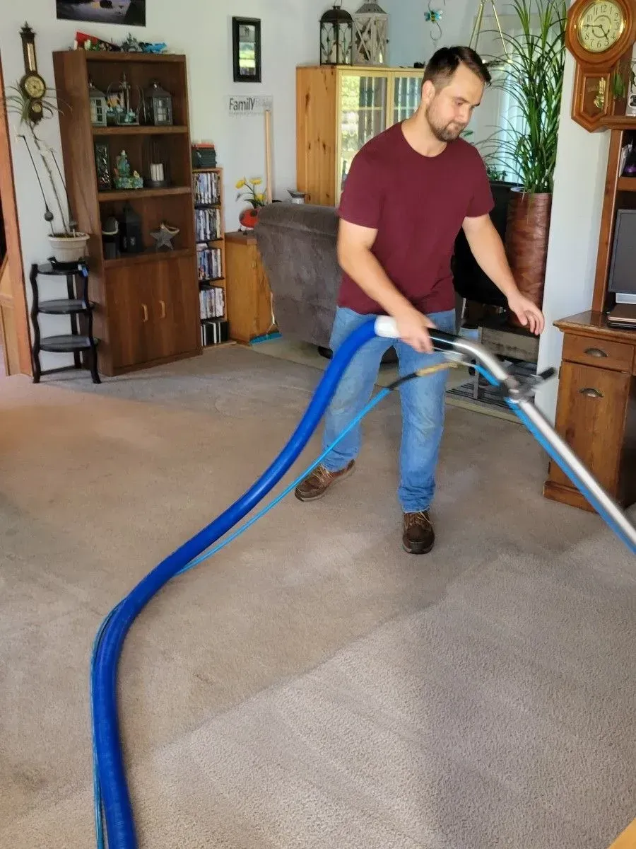 A man is using a vacuum cleaner to clean a carpet in a living room.