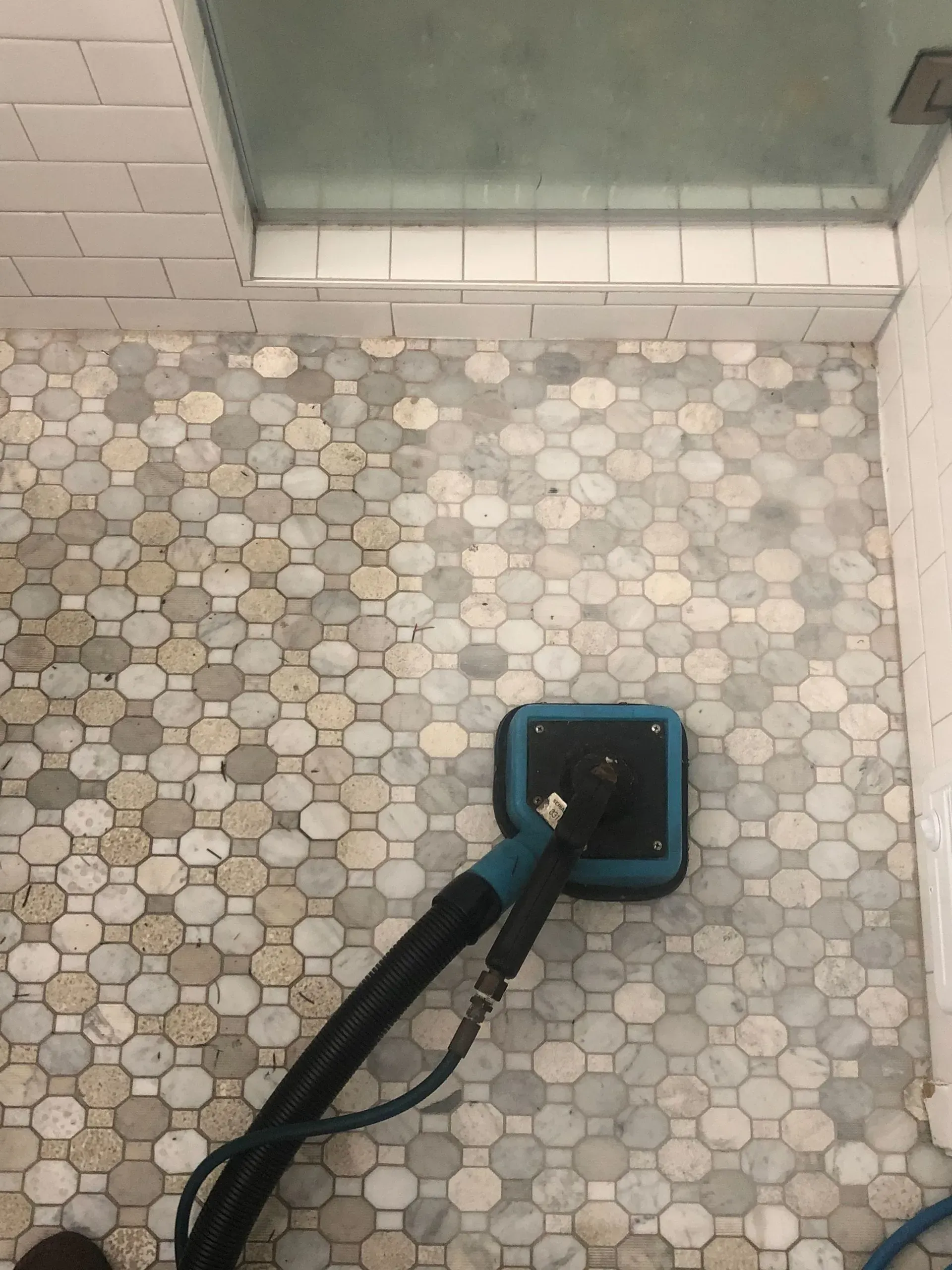 A vacuum cleaner is cleaning a tiled floor in a bathroom.