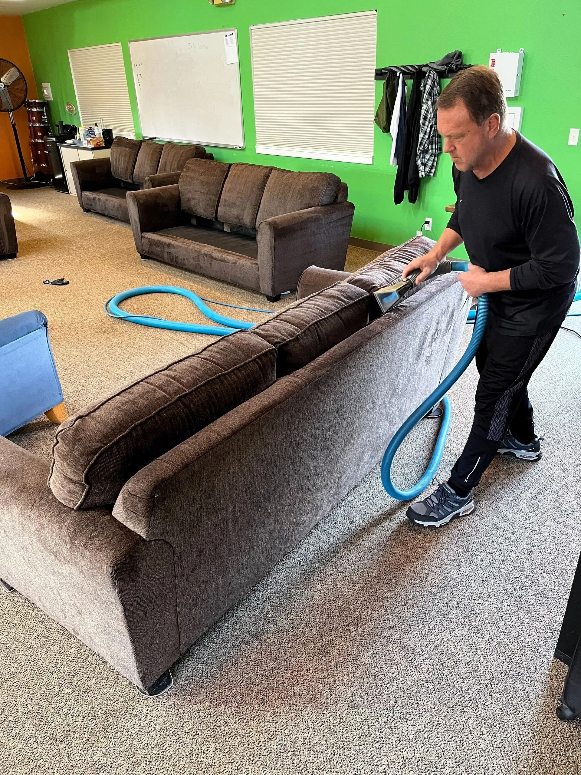 A man is cleaning a couch with a vacuum cleaner in a living room.