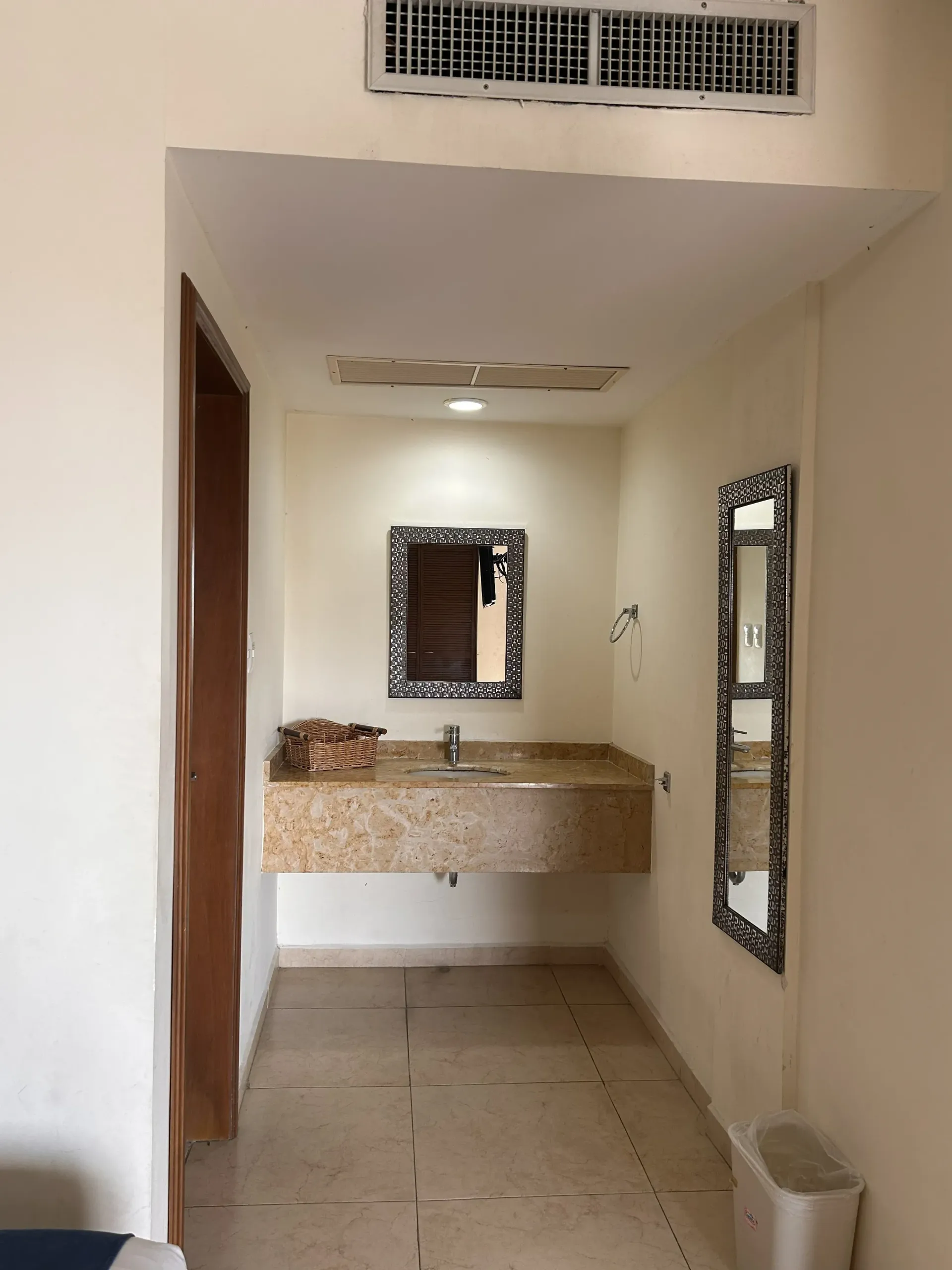 Un tocador de baño con encimera de piedra, espejo cuadrado, espejo rectangular alto y suelo de baldosas de color claro.