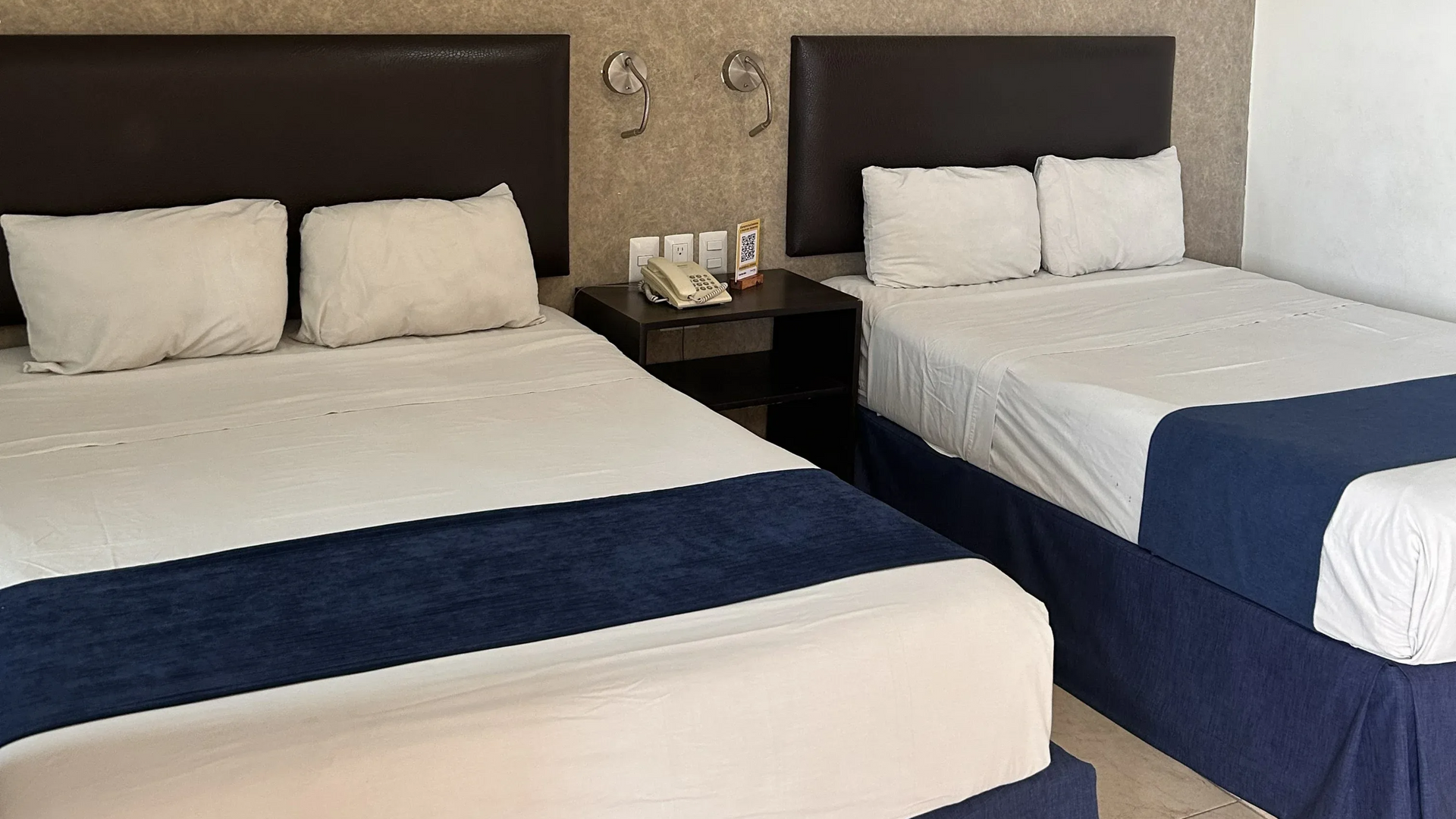 Dos camas tamaño queen con sábanas blancas y caminos de mesa azul oscuro.