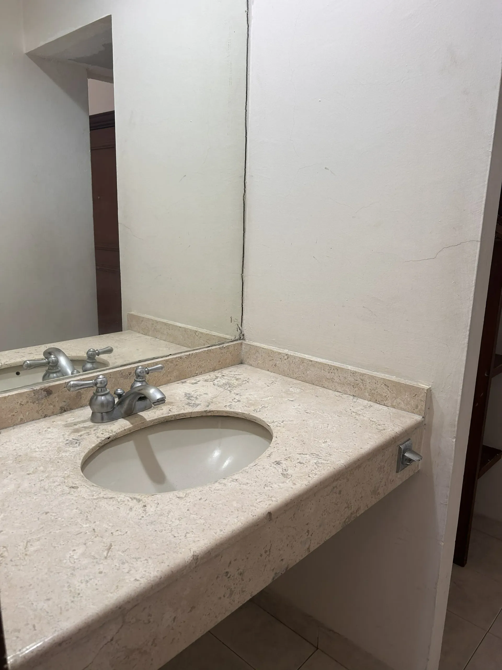 A bathroom vanity with a speckled beige stone countertop, an oval undermount sink, a chrome faucet, and a large mirror.