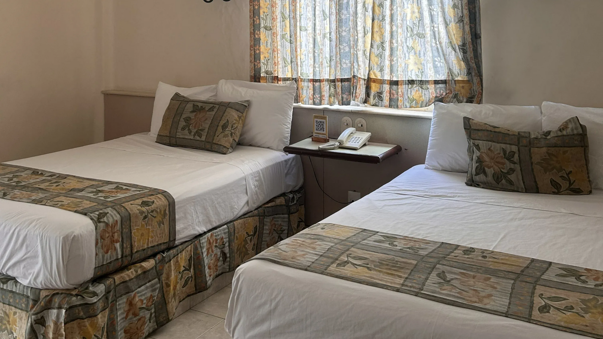 Una habitación de hotel con dos camas blancas adornadas con caminos de mesa estampados.