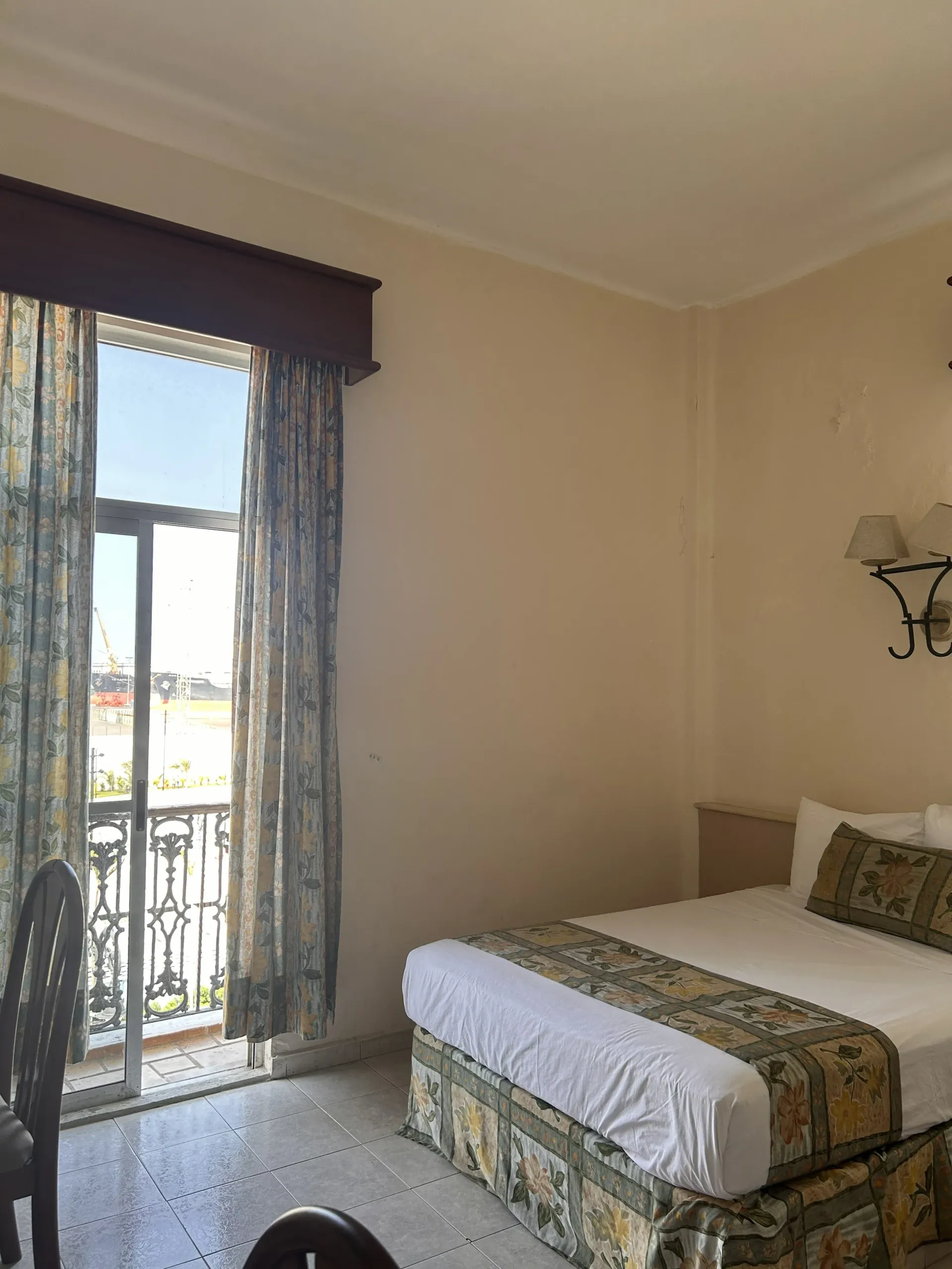 Una habitación de hotel con una cama blanca, ropa de cama estampada.