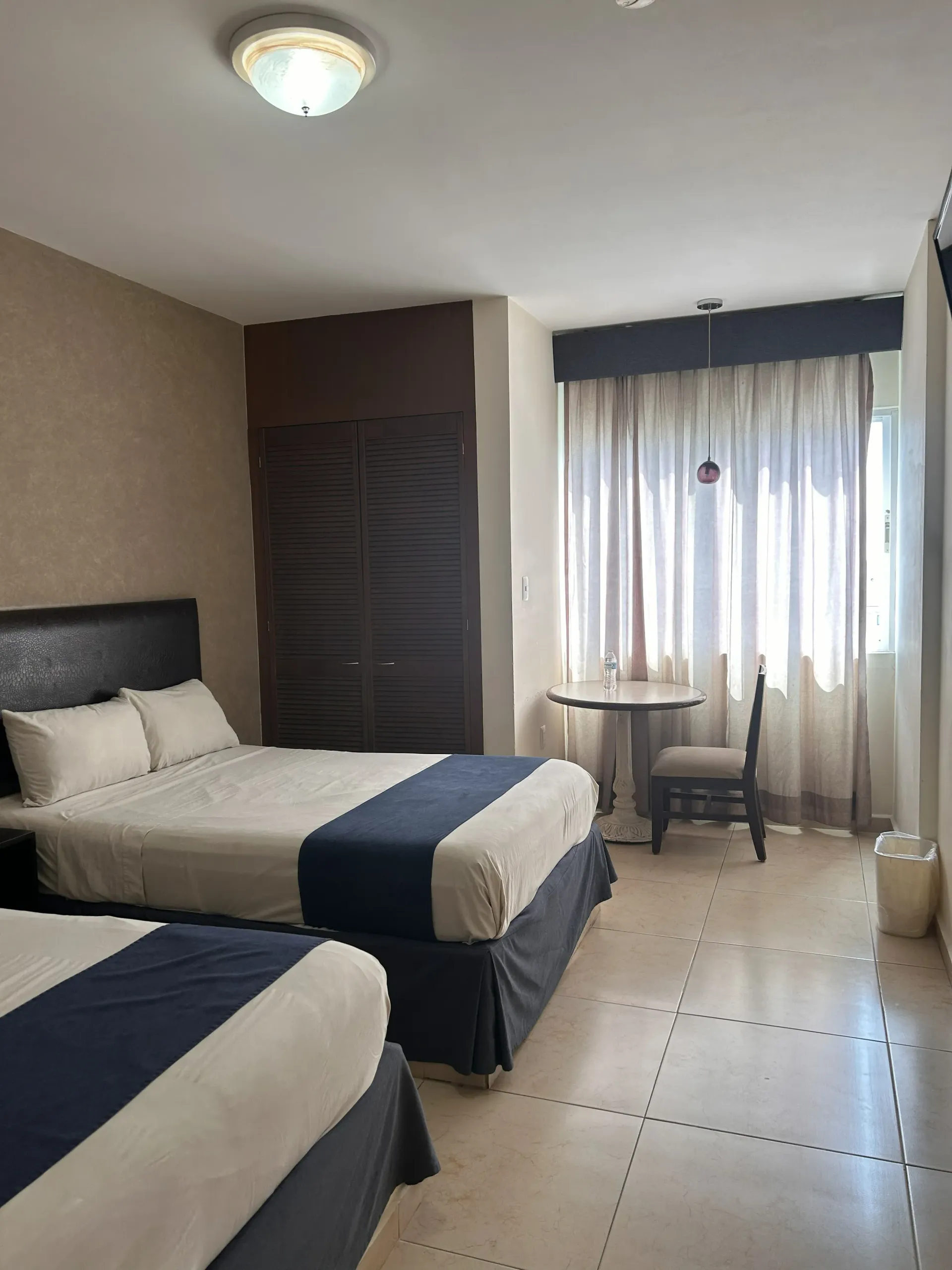 Una habitación de hotel con dos camas, un armario de color marrón oscuro, una pequeña mesa.