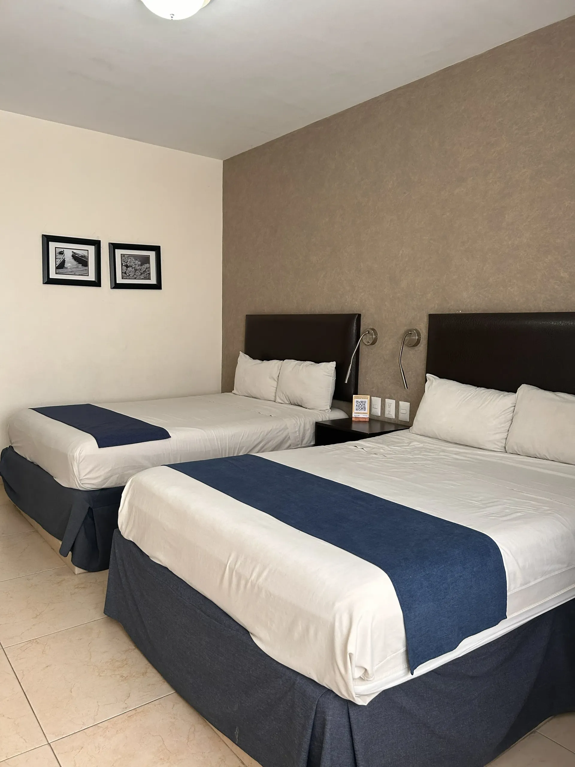 Una habitación de hotel con dos camas tamaño queen, con ropa de cama blanca, caminos de mesa azul marino.