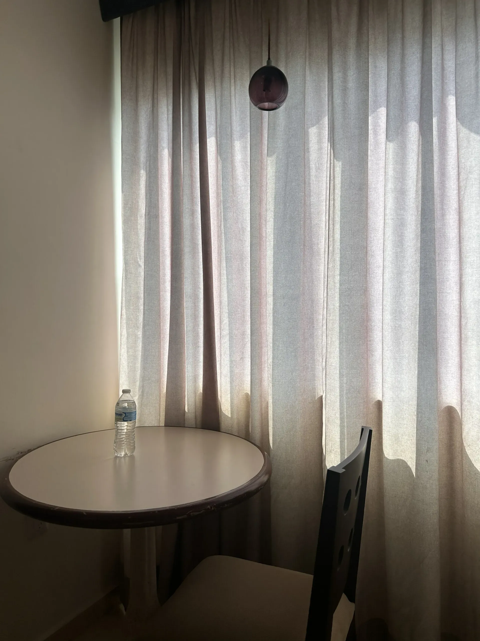 Una mesa redonda con una botella de agua y una silla junto a unas cortinas transparentes.