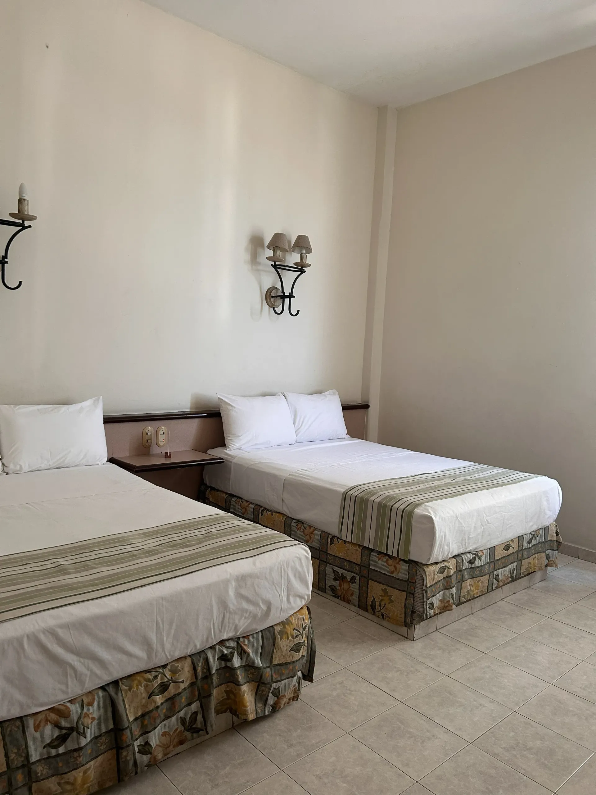 Dos camas individuales con sábanas blancas y faldones estampados en una habitación.