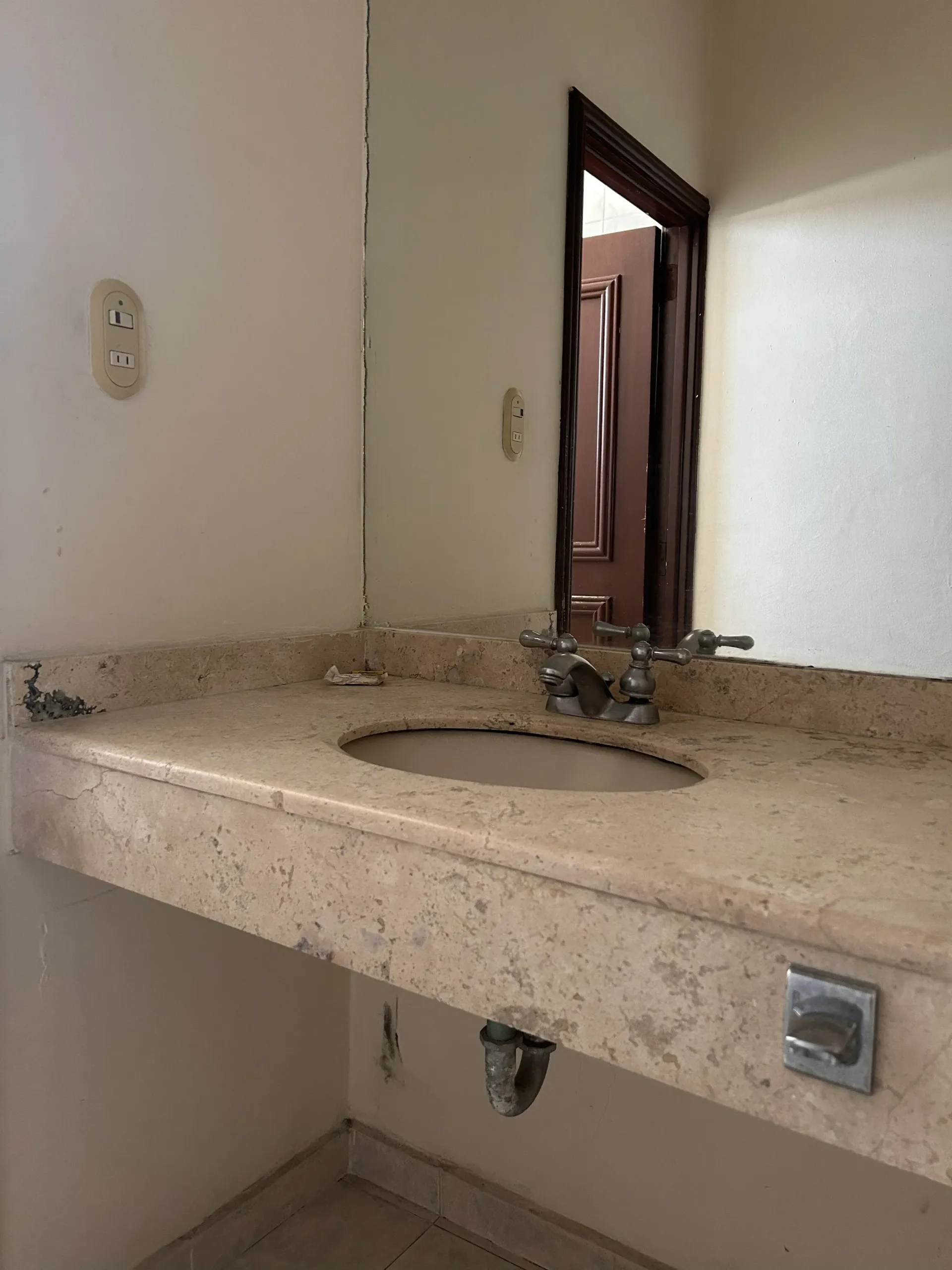Un mueble de baño de piedra con lavabo y grifo de metal, con un espejo montado en la pared encima.