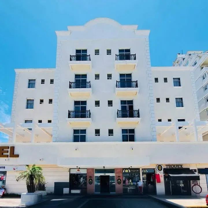 Una fachada blanca de hotel de varias plantas con balcones simétricos, bajo un cielo azul brillante.
