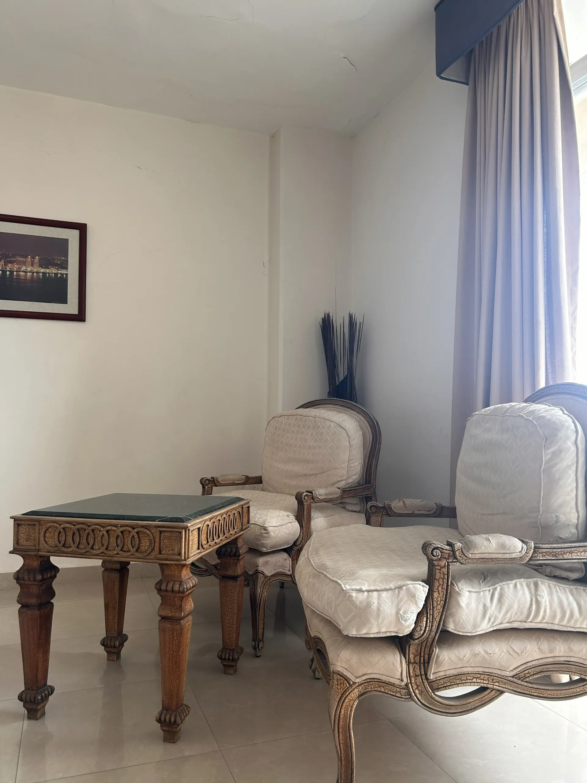 Dos sillones tapizados de estilo vintage y una pequeña mesa de madera ornamentada en una habitación.