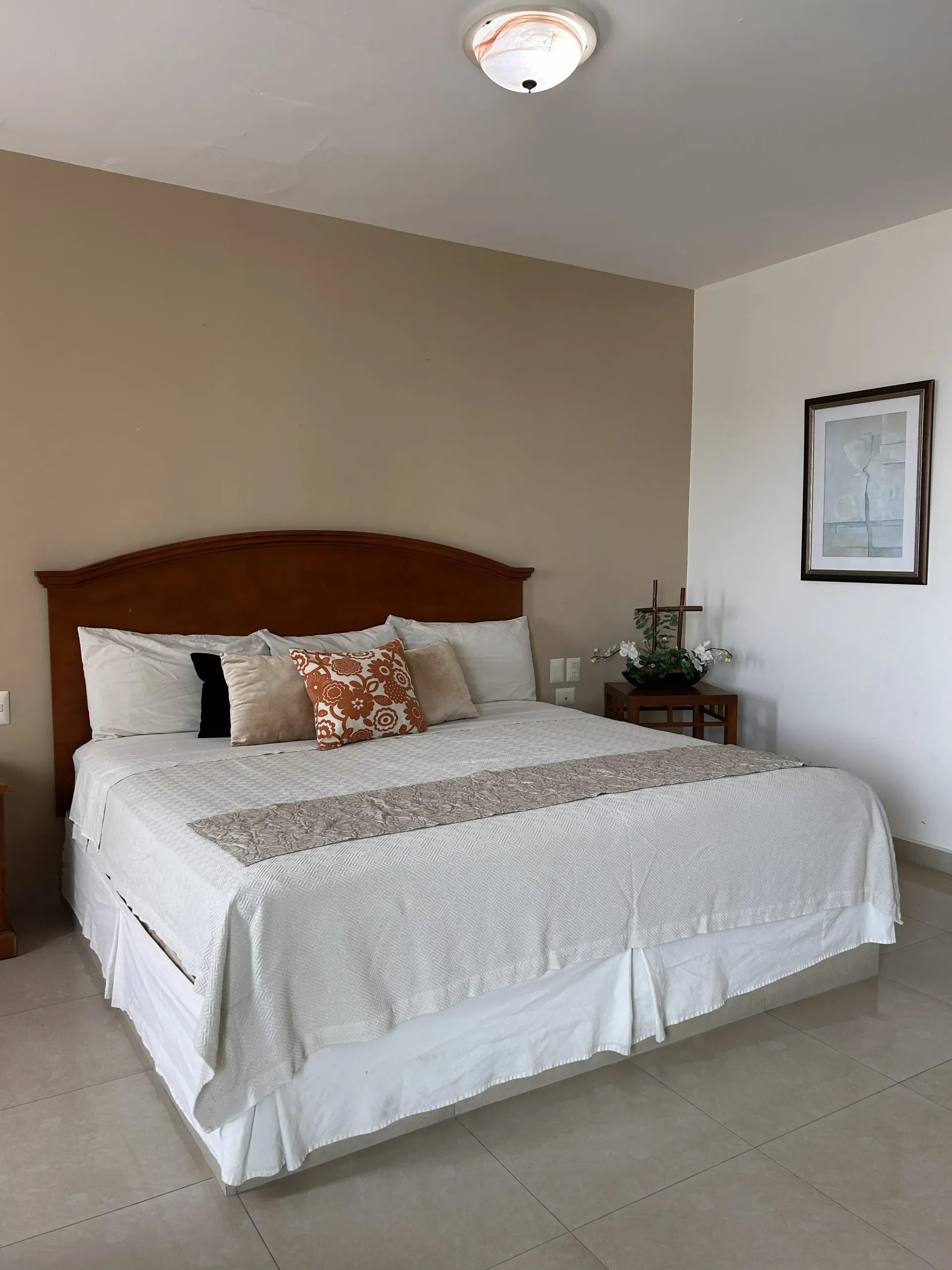 Una cama tamaño king con ropa de cama blanca, almohadas y un cojín decorativo con estampado.