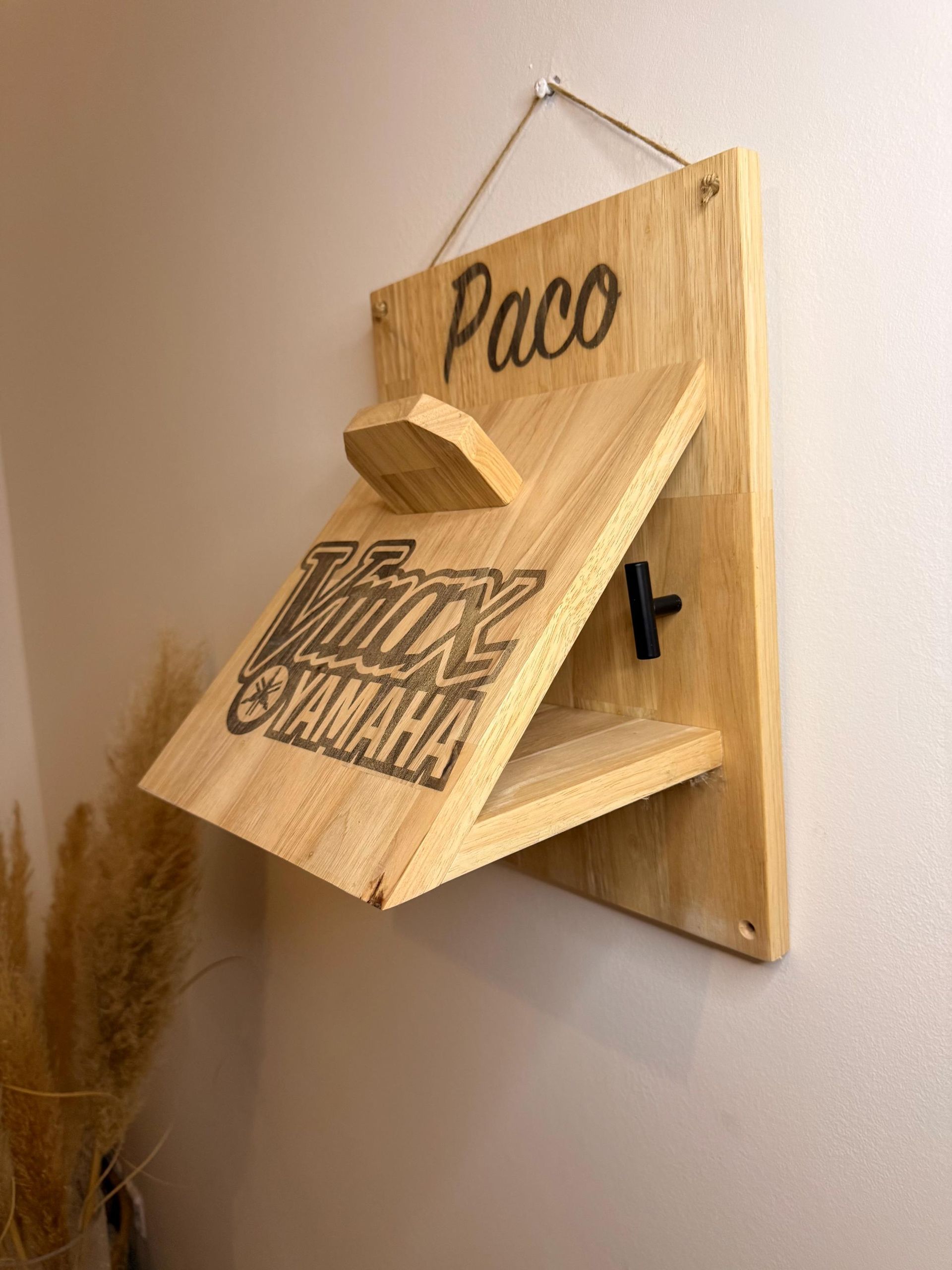 Bicicleta colgada en un estante de madera fijado a la pared, con un casco y ganchos. Fondo de pared a rayas verdes y blancas.