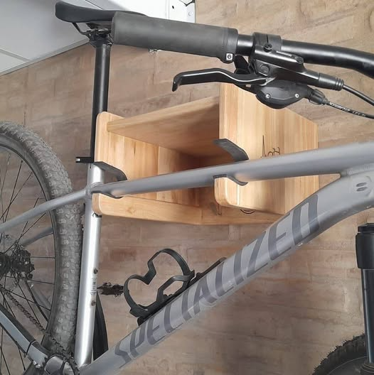 Una bicicleta montada sobre un estante de madera en la pared. Cuadro gris, manillar negro y portabotellas.