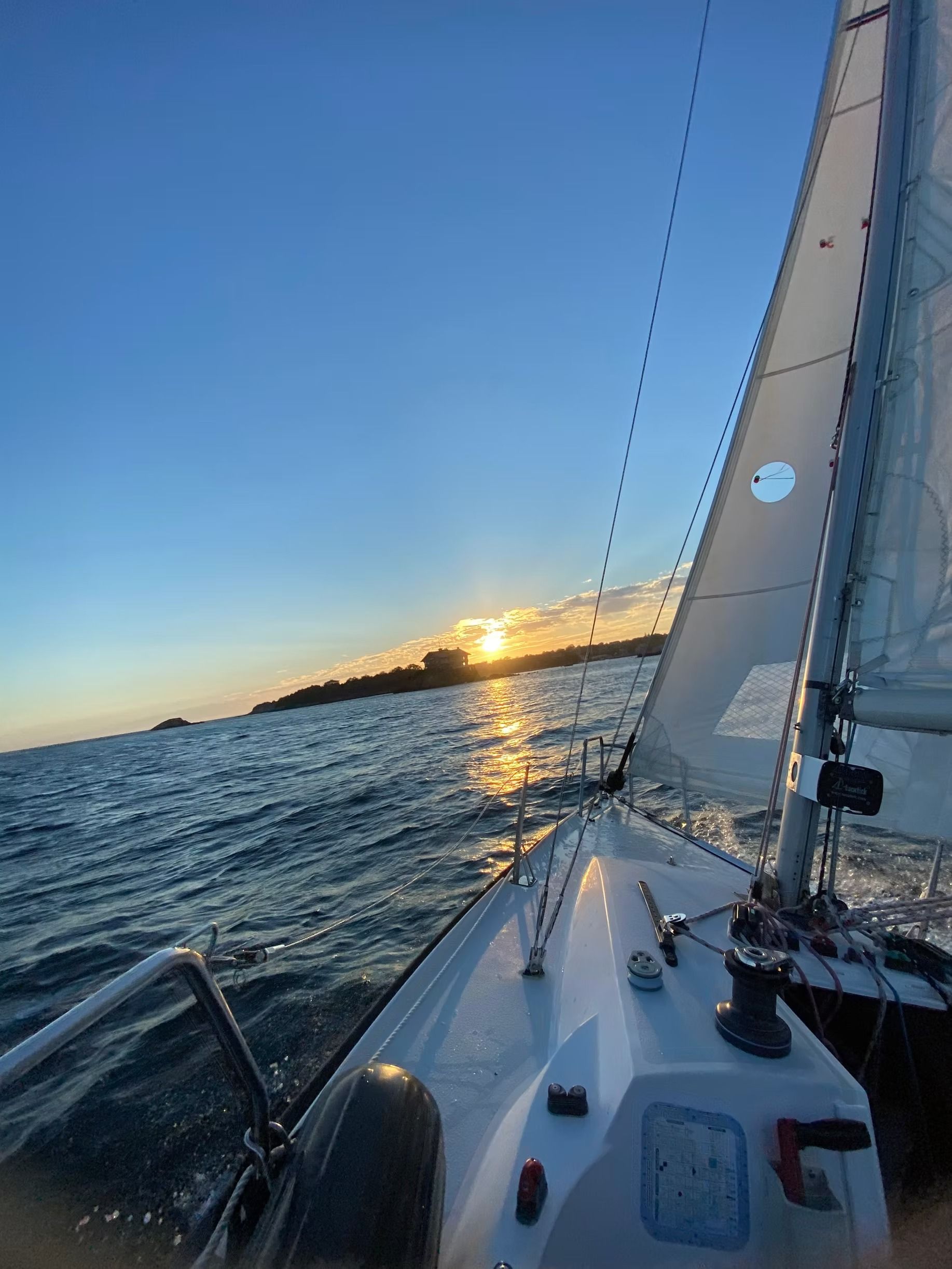 A sailboat gliding across the water toward a horizon at sunset, with the sail partially visible on the right.