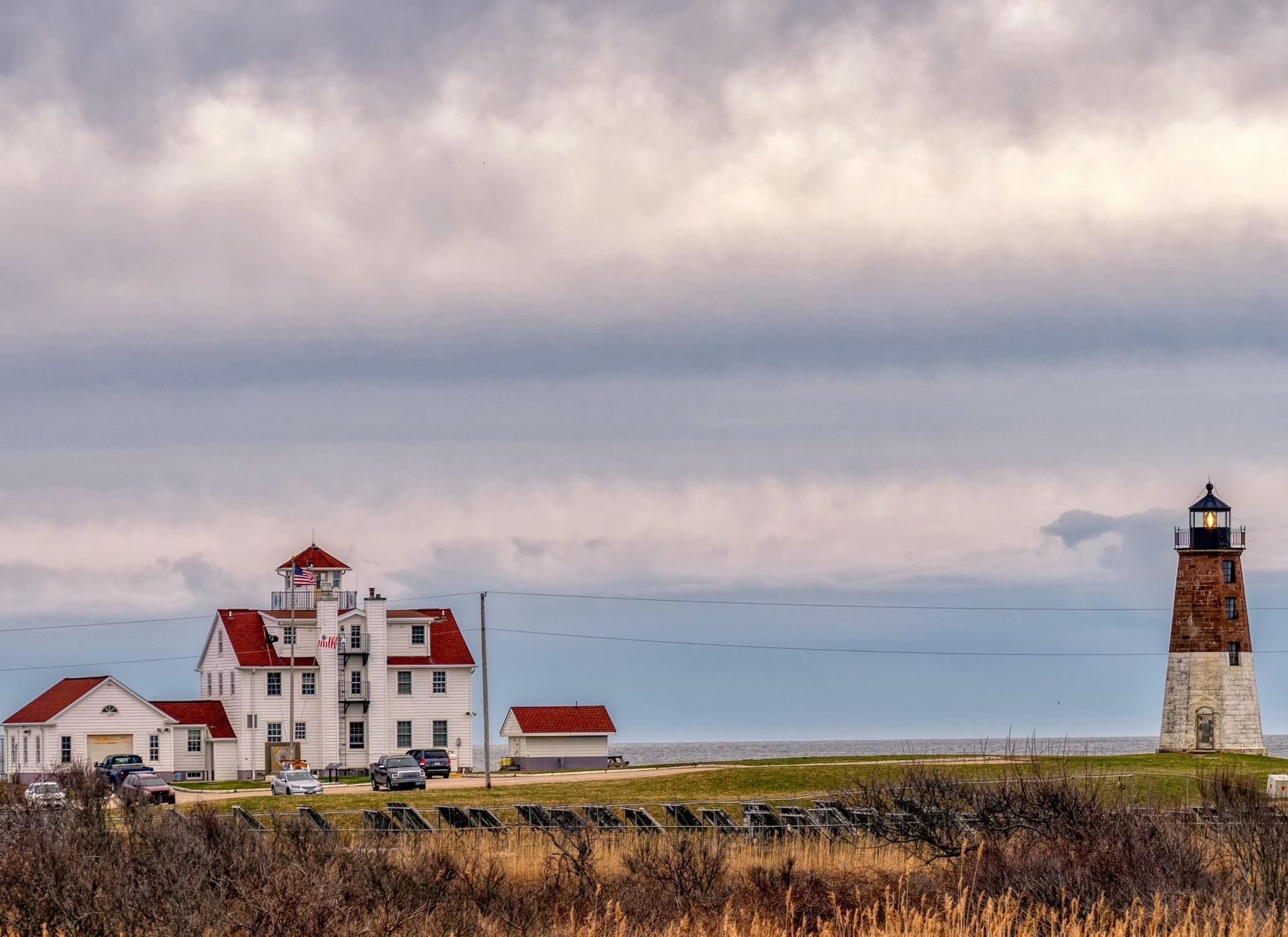 Point Judith Lighthouse with its adjacent buildings under a cloudy, overcast sky near the ocean.