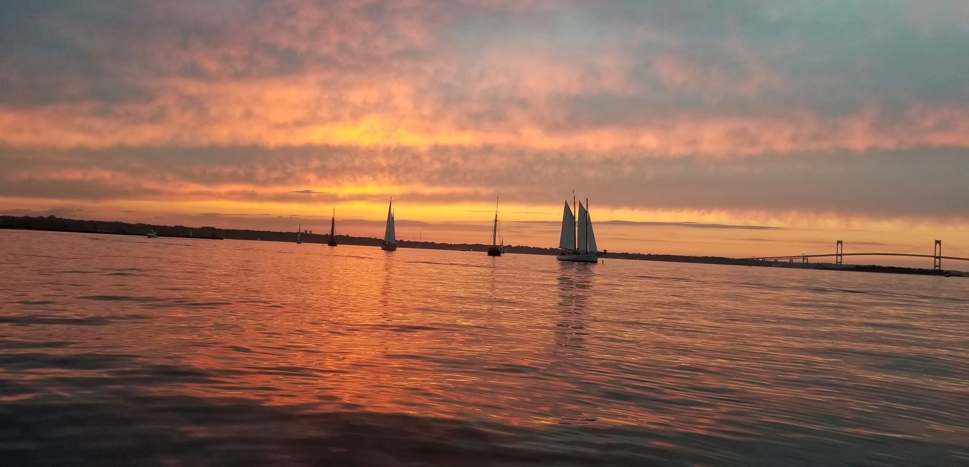 A silhouette of sailboats on the water during a vibrant orange and pink sunset.