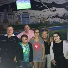 Group of people posing together in front of a mural, smiling.