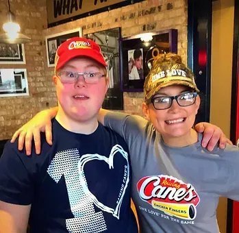 Two people in Raising Cane's restaurant, posing with arms around each other.