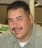 Man with short dark hair and mustache smiling in a light green shirt.