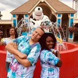 People posing in front of a fountain with a Snoopy statue, wearing tie-dye shirts.