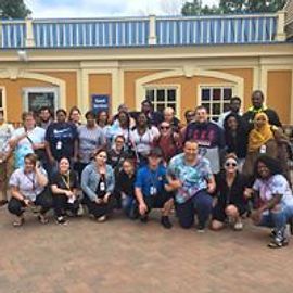 Group of people standing outside a yellow building with blue trim.