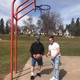 Two people play basketball on an outdoor court. One holds the ball; the other points.