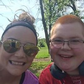 Woman with sunglasses and boy smiling outdoors, trees in background.