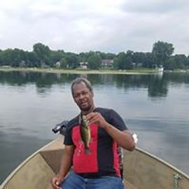 Man in boat holding a small fish, on a lake, cloudy sky.