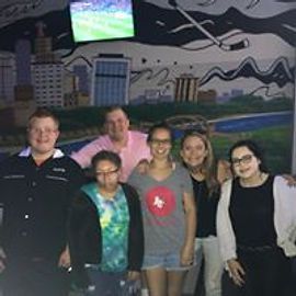 Group of six people posing in front of a mural, some smiling, with colorful shirts.