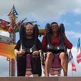 Two people on a slingshot ride at an amusement park. They are strapped in, smiling, and appear excited.