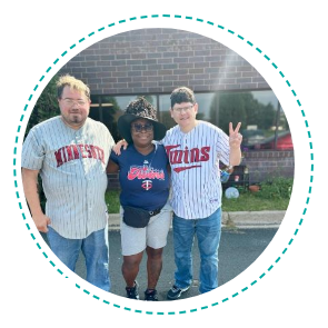 Three people in Twins baseball jerseys smile outdoors. Building in the background.