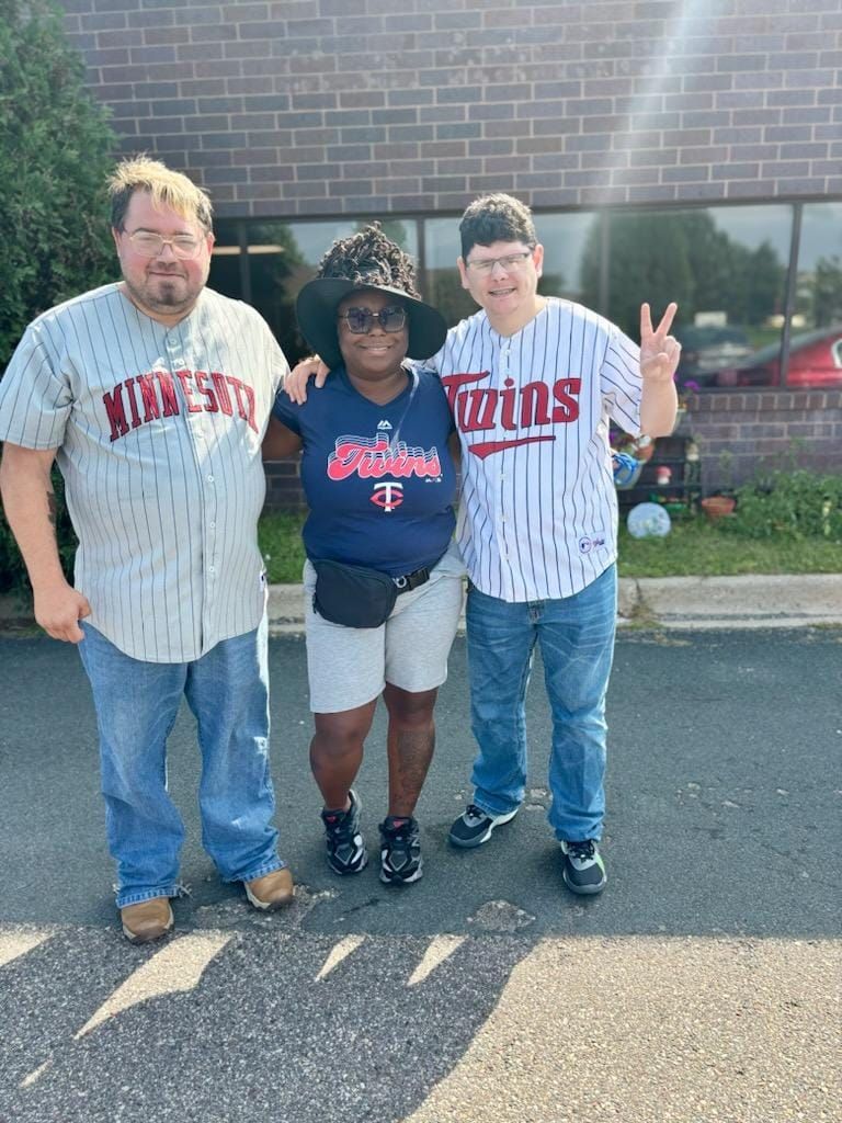 Three people pose together outdoors, all wearing Minnesota Twins baseball apparel.